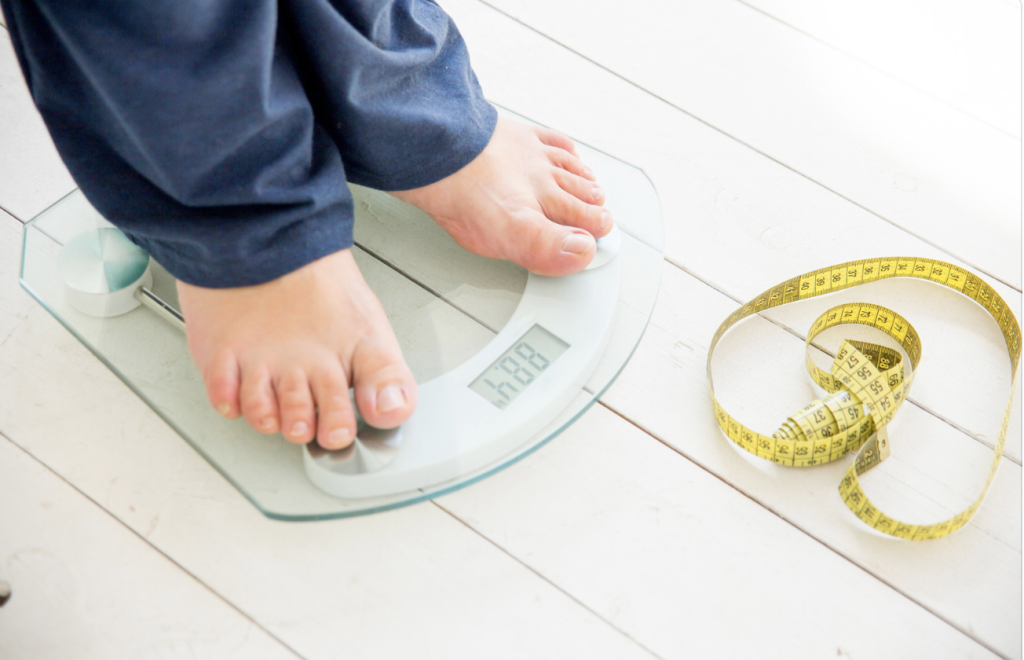 A woman standing on a scale monitoring her weight. Weight gain or loss in excess can cause abnormal bleeding. 